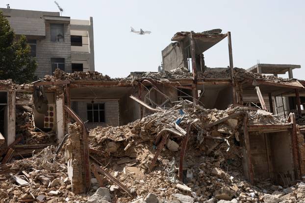 An airplane flies across the sky over a building, which was damaged in a U.S. and Israeli strike in March, in Tehran
