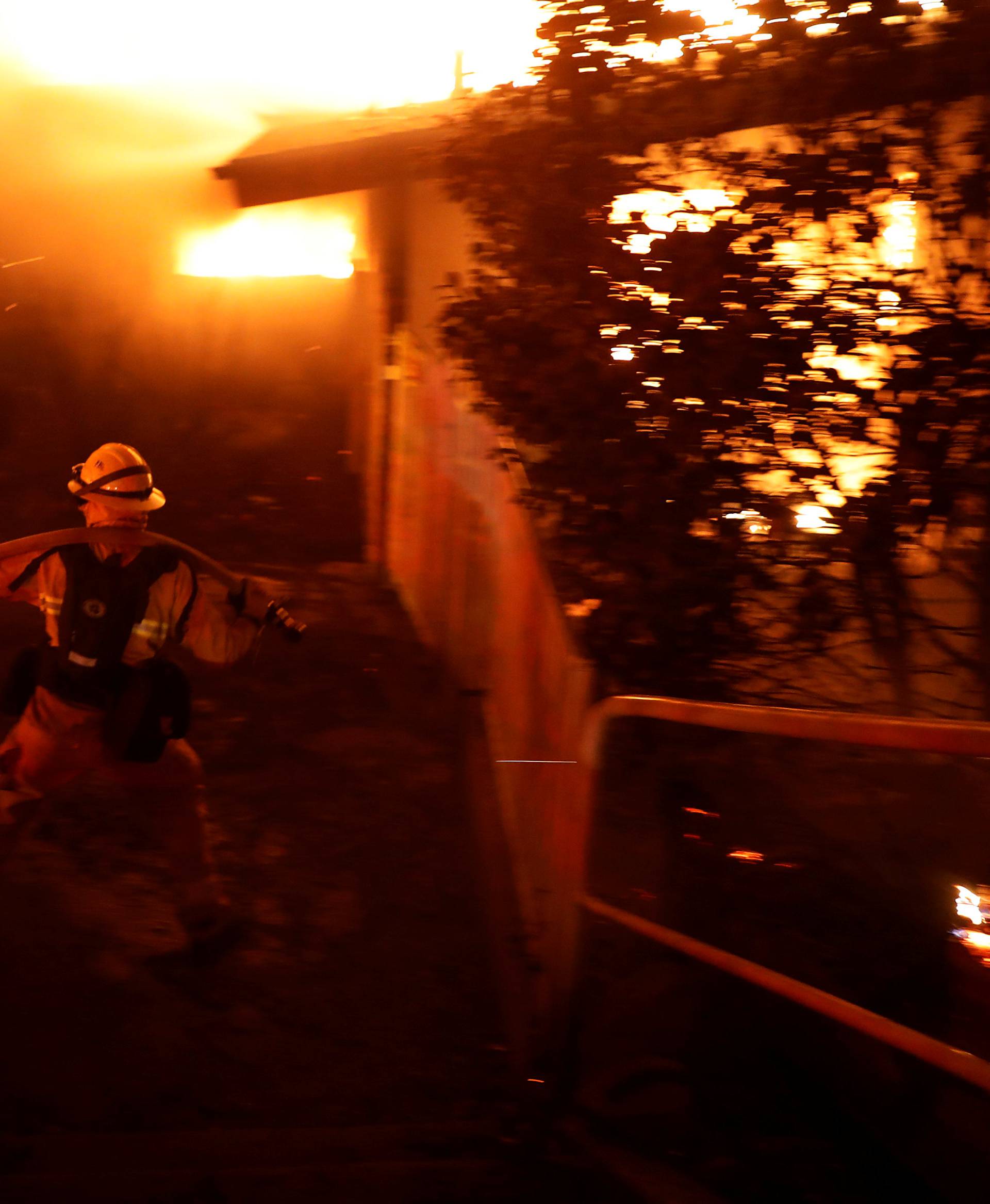 A firefighter drags a hose as he battles the Camp Fire in Paradise