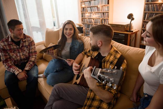 Group of friends on a house party playing guitar and enjoying music