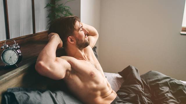 Carefree guy enjoying new day. Sexy, happy bearded man in bed