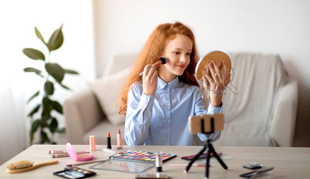 Teen applying face powder, recording beauty blog on smartphone