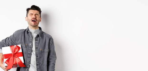 Valentines day heartbreak. Single and heartbroken guy crying lonely, holding big gift box, being rejected by lover, sobbing and feeling alone, standing on white background