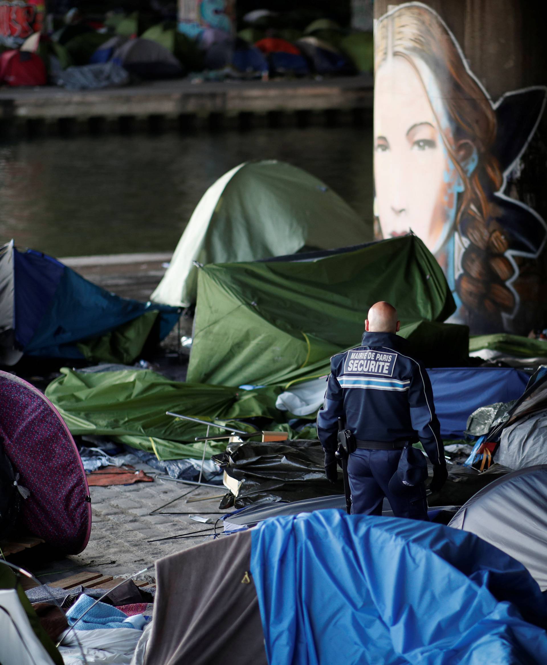 A municipal security guard stands in the midst of abandoned tent and belongings as French police evacuate hundreds of migrants living in tents along a canal in Paris