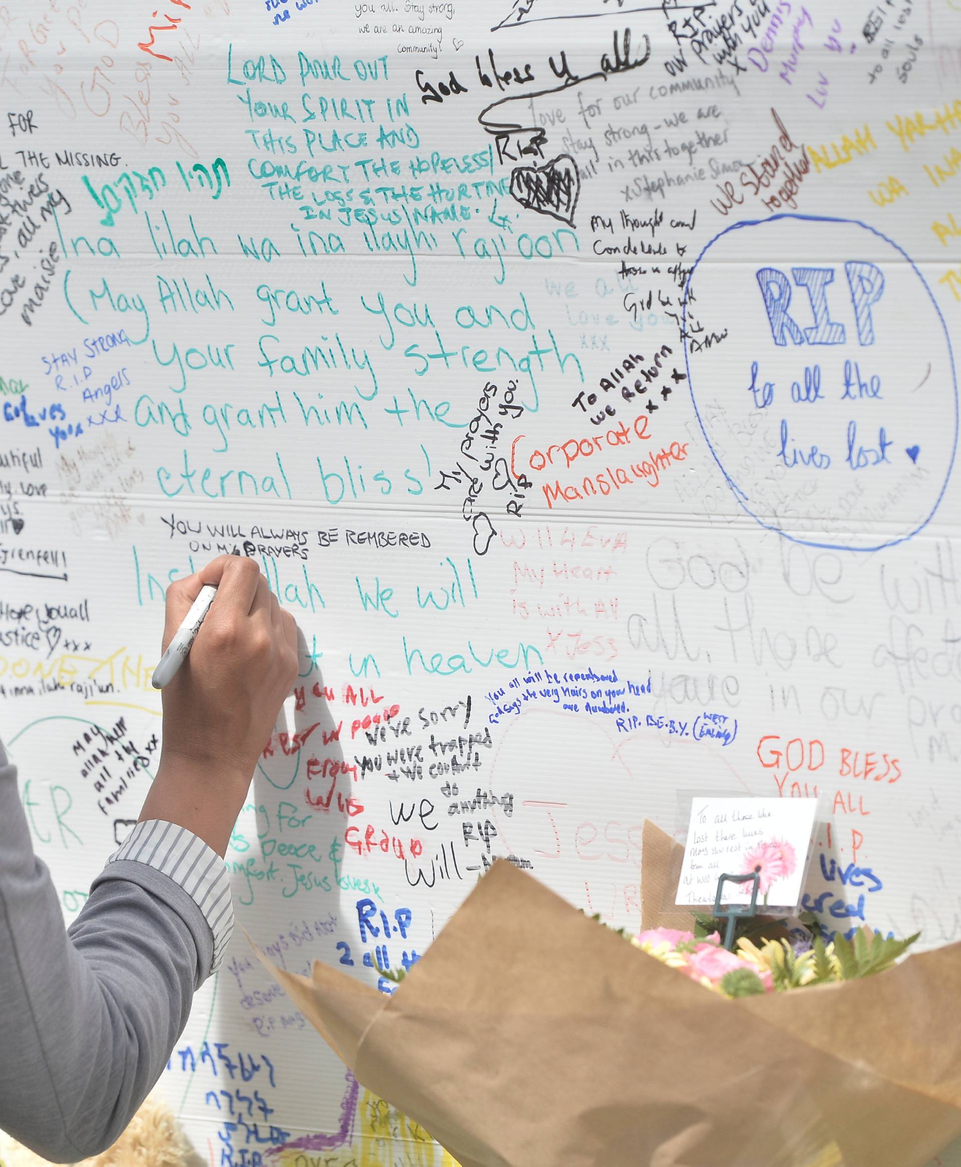 A woman writes on a message wall following the fire that destroyed the Grenfell Tower block, in north Kensington, West London