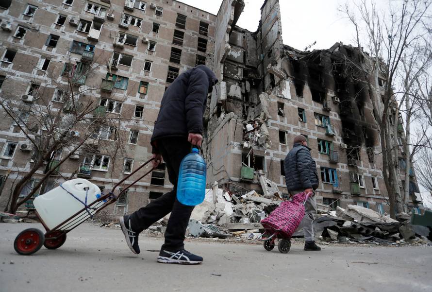 Local residents walk past a damaged apartment building in Mariupol