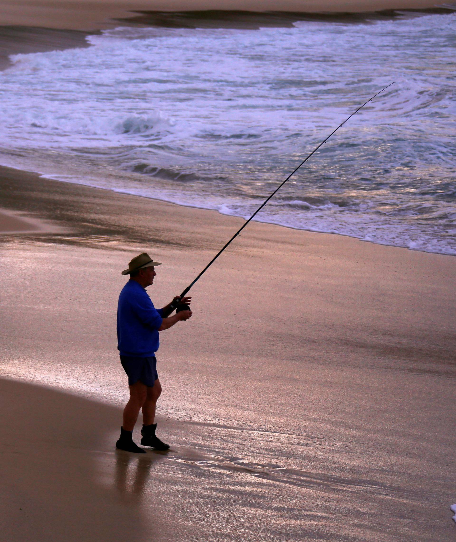 A fisherman stands on the edge of the surf after casting his line at sunset on Sydney's Bronte Beach, Australia