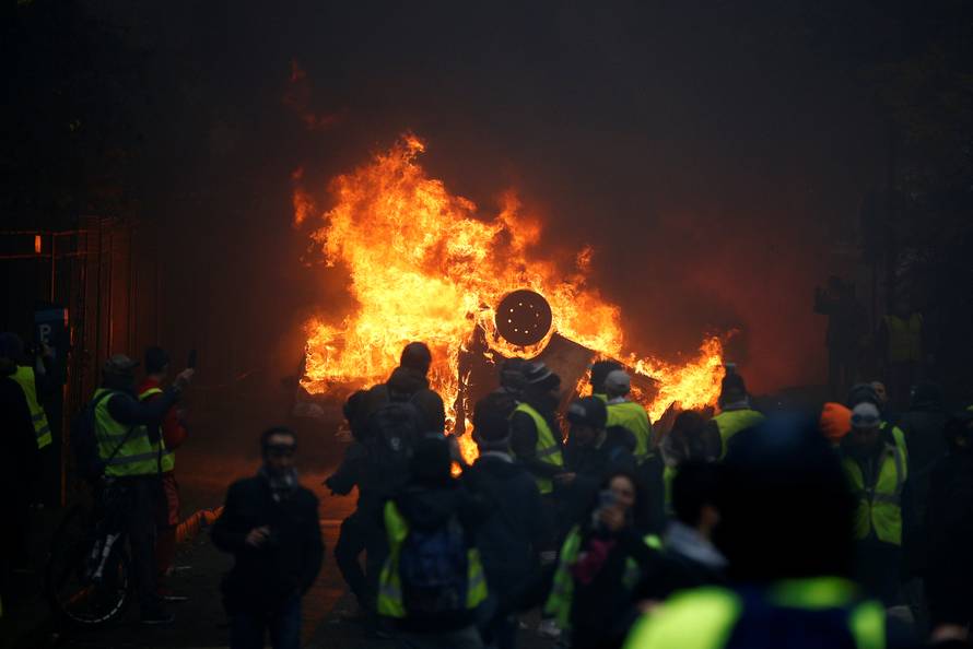 Protesters wearing yellow vests, a symbol of a French drivers' protest against higher diesel fuel taxes, gather near a burning car during clashes near the Place de l'Etoile in Paris