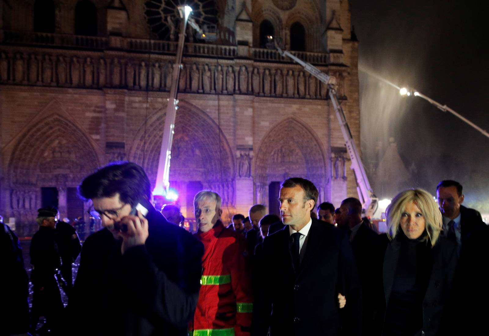 French President Emmanuel Macron and his wife Brigitte walk outside the Notre Dame Cathedral where a fire burns in Paris