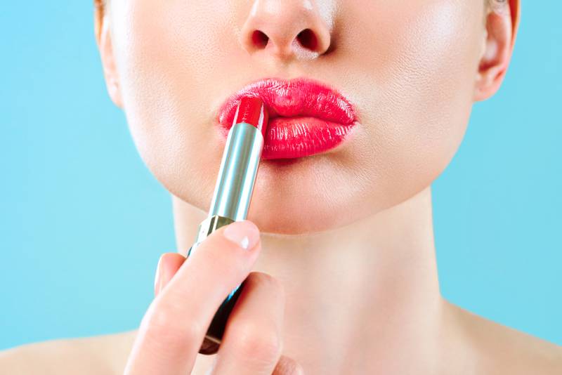 Beautiful woman paints lips with lipstick. Beautiful woman face. Makeup detail. Beauty girl with perfect skin. Red lips and health skin. The concept of beauty, glamor and passion