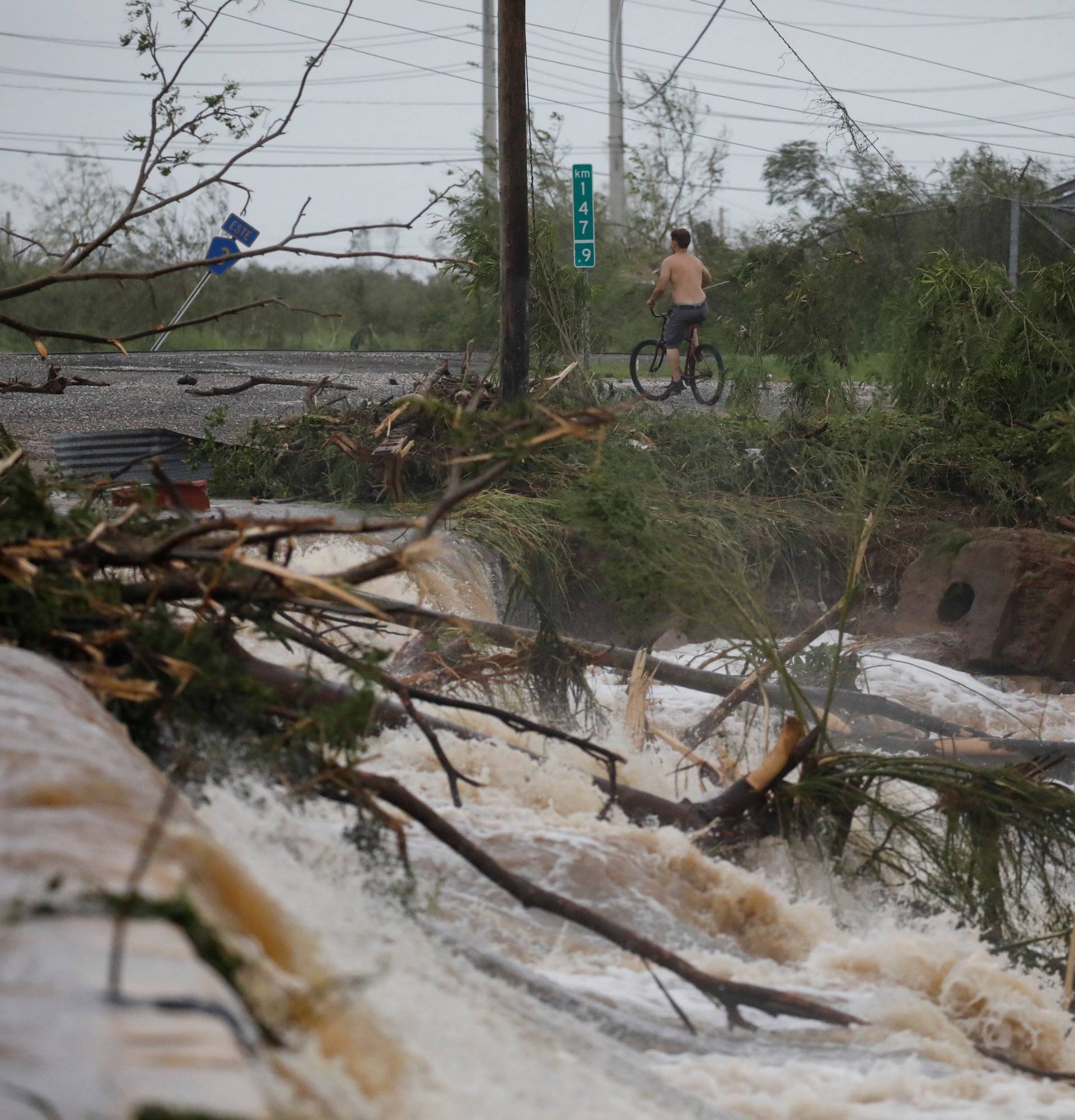 A man rides a bicycle next to a flooded road after the area was hit by Hurricane Maria en Guayama