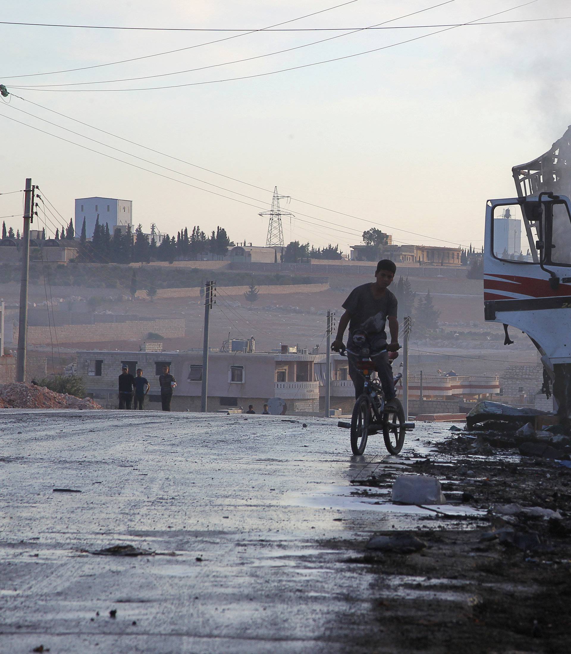 A boy rides a bicycle near a damaged aid truck after an airstrike on the rebel held Urm al-Kubra town