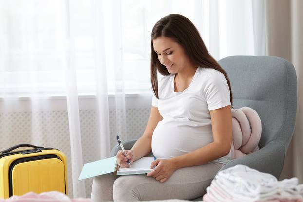 Pregnant woman writing packing list for maternity hospital at ho