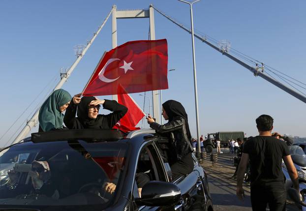 Women wave Turkish flags after troops involved in the coup surrendered on the Bosphorus Bridge in Istanbul