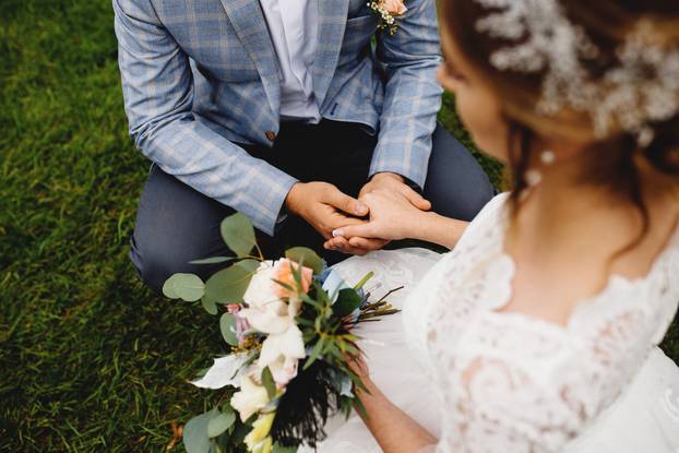 Bride in white dress is holding wedding bouquet. Groom is holding her hand