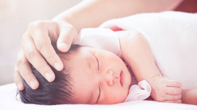Mother hand touching asian newborn baby girl head while she slee