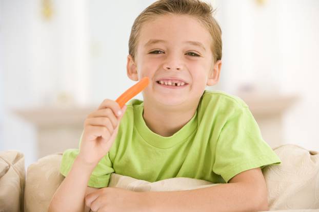 Young boy eating carrot stick in living room smiling