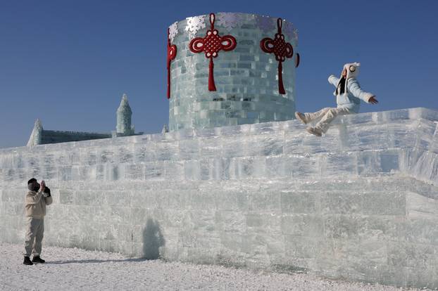 A person poses on an ice wall at the annual Ice and Snow Festival in Harbin