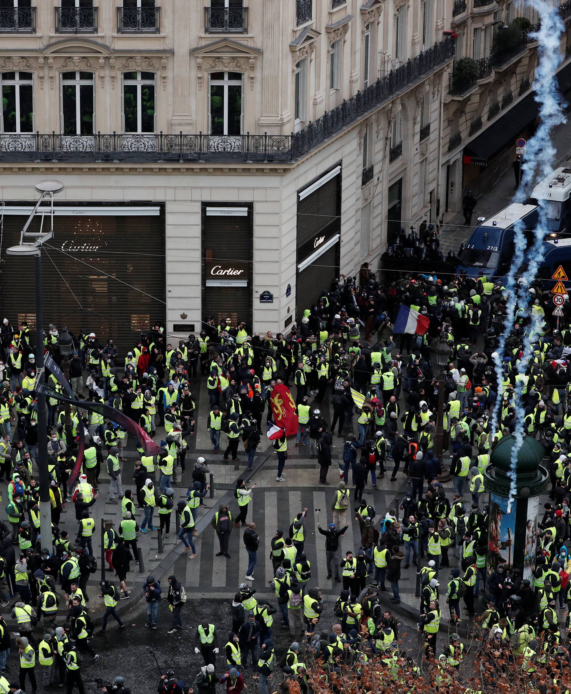 Tear gars floats in the air around protesters wearing yellow vests during clashes with French Gendarmes on the Champs-Elysees Avenue in Paris