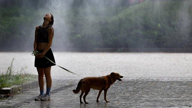 Woman with a dog cools herself under a water sprinkler on an extremely hot summer day in Kyiv