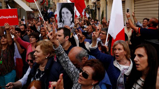 A demonstrator carries a photo of assassinated anti-corruption journalist Daphne Caruana Galizia as others sing the national anthem at the end of a protest against government corruption revealed by the Daphne Project, in Valletta