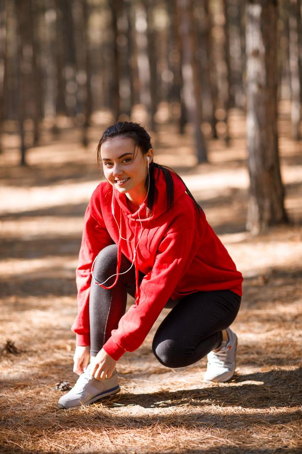 Girl tying shoelaces in the forest during training. Concept photo, close-up