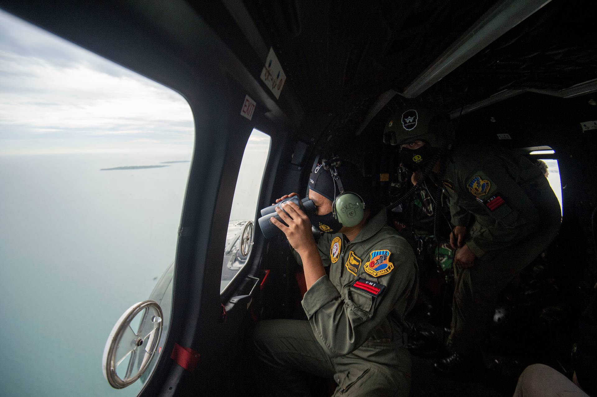 An Indonesian Air Force personnel looks through the window of NAS-332 Super Puma helicopter during an aerial search for the Sriwijaya Air SJ-182, which crashed to the sea