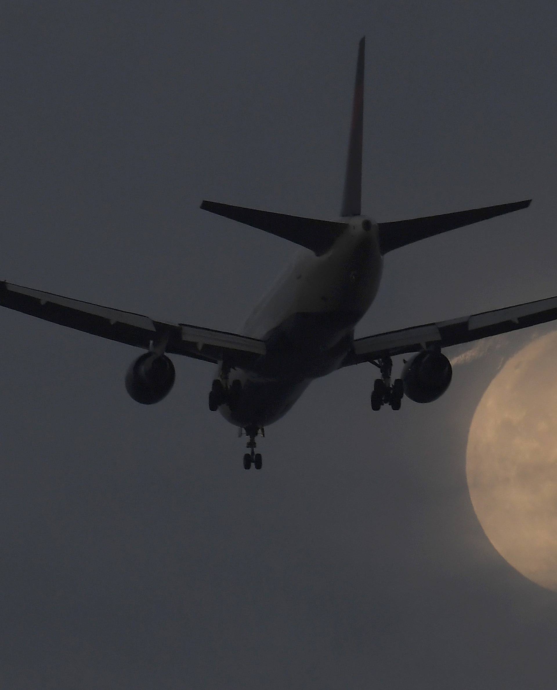 A passenger aircraft makes it's landing approach to Heathrow airport in front of a "super moon" at dawn in west London