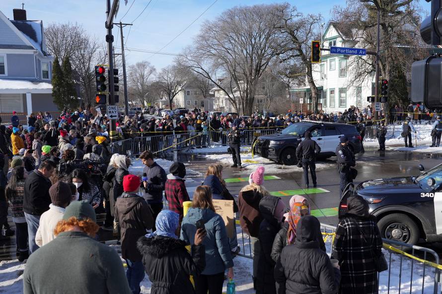 Members of the community gather as police officers block the scene after the driver of a vehicle was shot, in Minneapolis