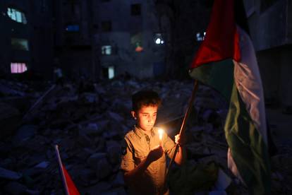 A boy holds a candle at the site of a house that was destroyed by Israeli air strikes during the Israeli-Palestinian fighting, in Gaza