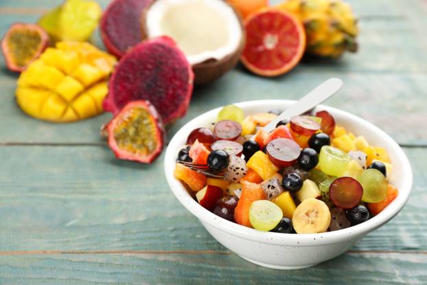 Delicious exotic fruit salad and ingredients on light blue woode