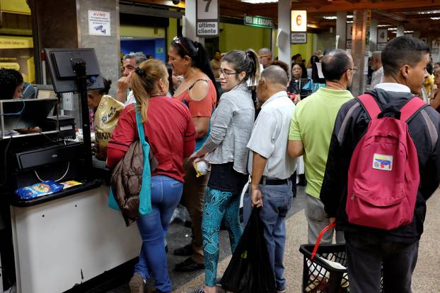 People queue to pay for food at the cashier of a supermarket in downtown Caracas