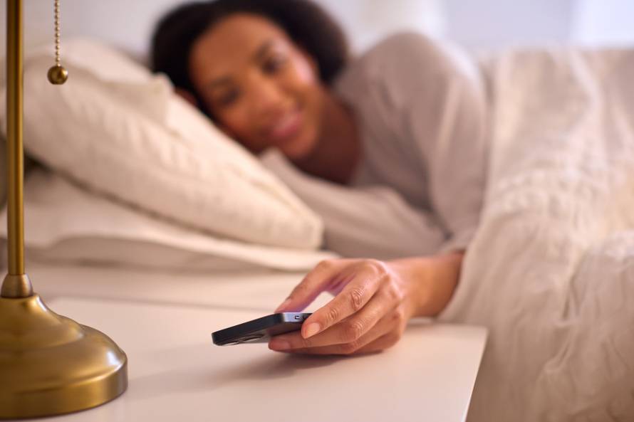 Woman At Home In Bed Turning Off Alarm On Mobile Phone