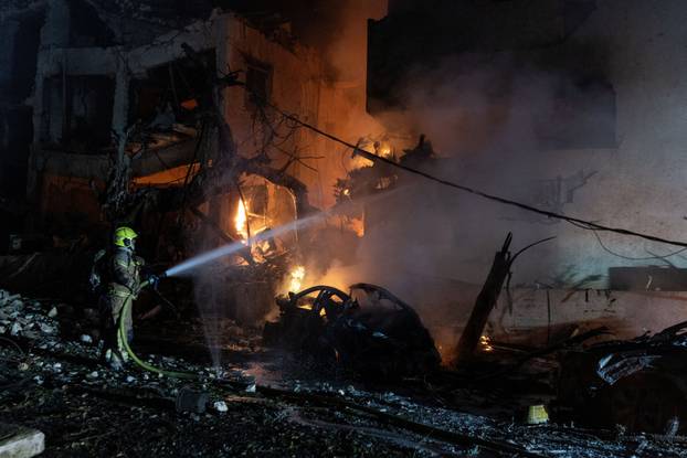 An Israeli firefighter works to put out a fire on a car at the site of a projectile impact, in Tel Aviv