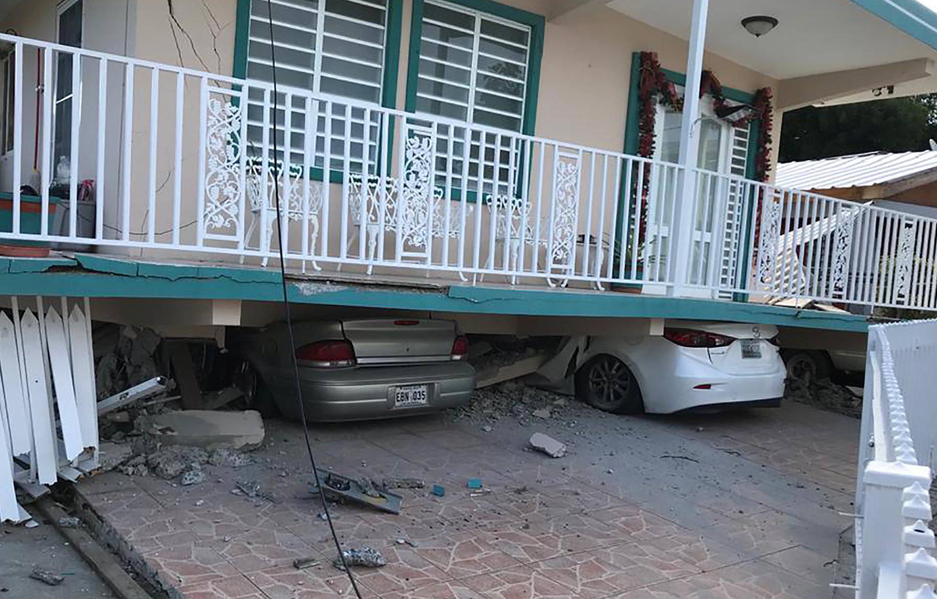 Cars lie under a collapsed house after an earthquake in Guanica
