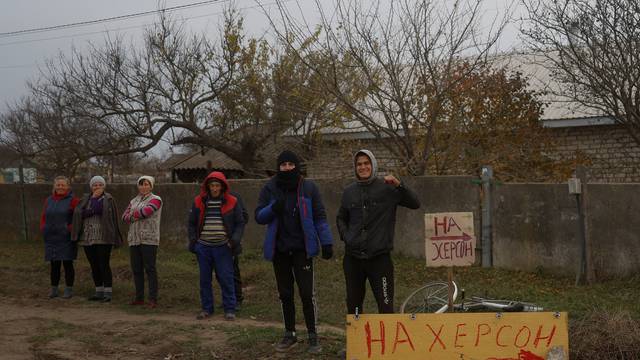 Residents of the village of Kyselivka, recently retaken by the Ukrainian Armed Forces, stand next to a make-shift road sign that points direction to Kherson city