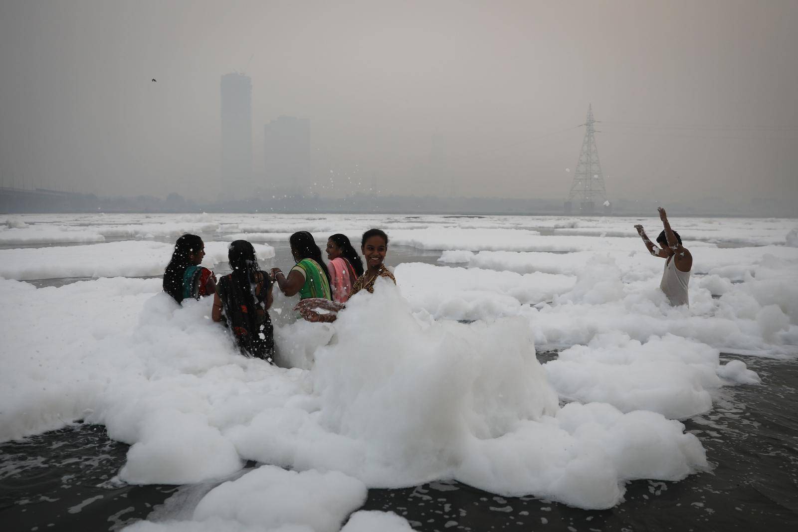 People bathe amidst the foam covering the polluted Yamuna river on a smoggy morning in New Delhi