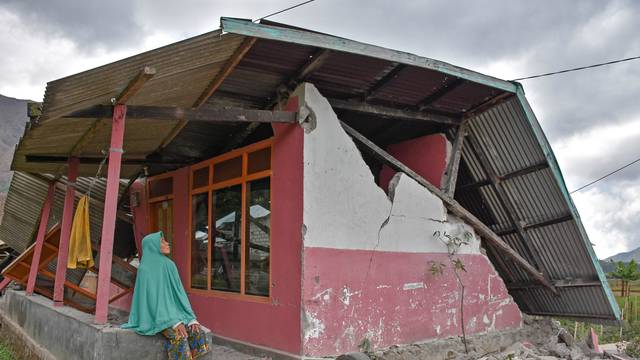 A villager sits at her damaged house after an earthquake hit Sembalun Bumbung village in Lombok Timur