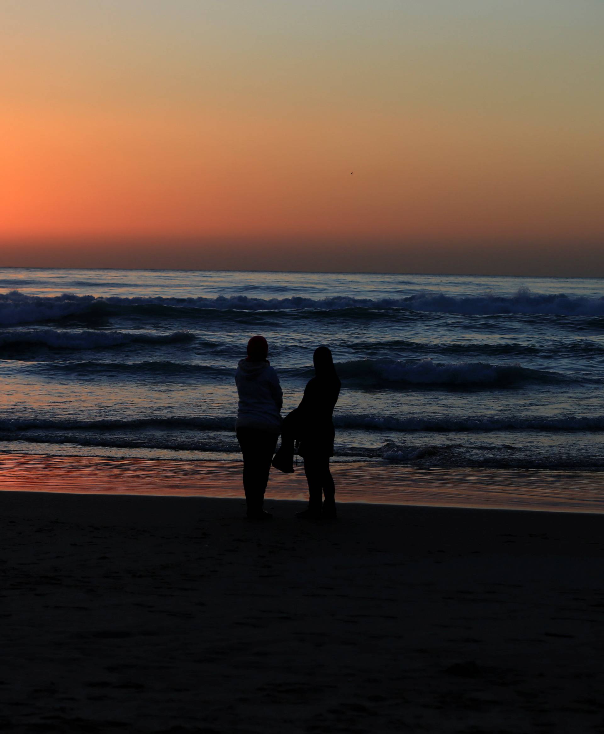 Two women watch the sunset over the Mediterranean sea on a cold day at a public beach in Beirut