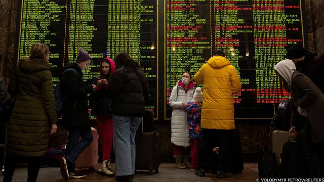 People stand in front of the train schedule at Central Railway Station as they try to leave Kyiv