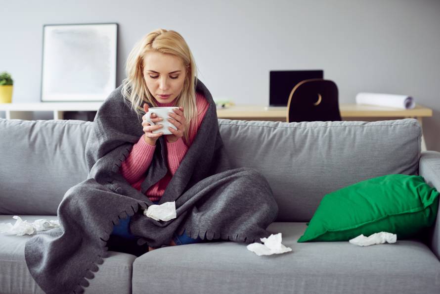 Young sick woman sitting on sofa drinking tea