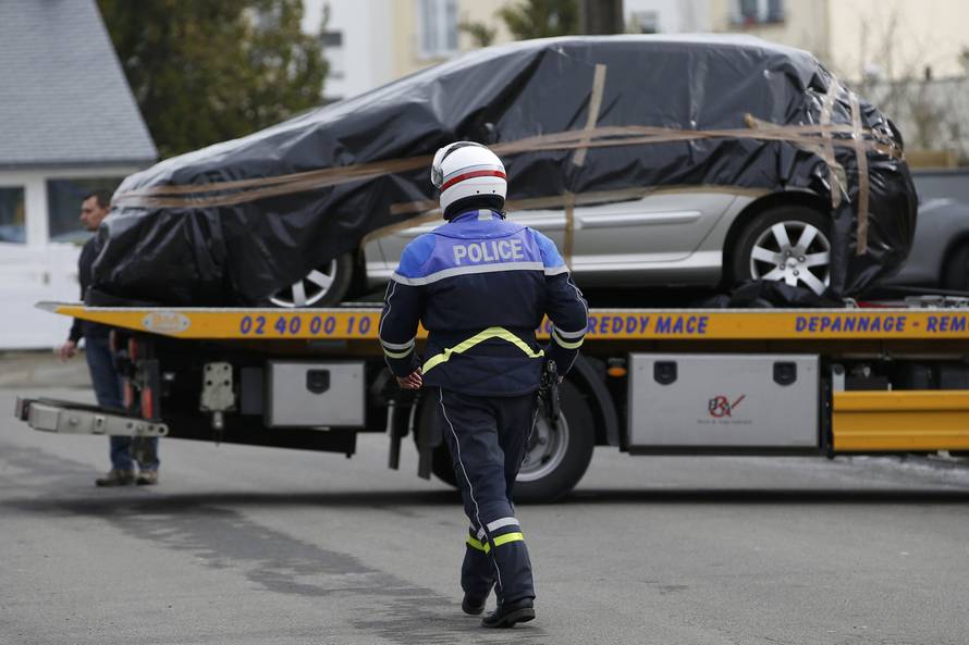 A French policeman walks towards the covered abandoned automobile of Sebastien Troadec in a parking lot in Saint Nazaire