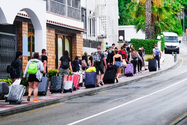 LLORET DE MAR, SPAIN - JULY 27, 2019: Group of tired tourists walks along the street with luggage to the hotel on the Costa Brava. The concept of rest. Summer travel.