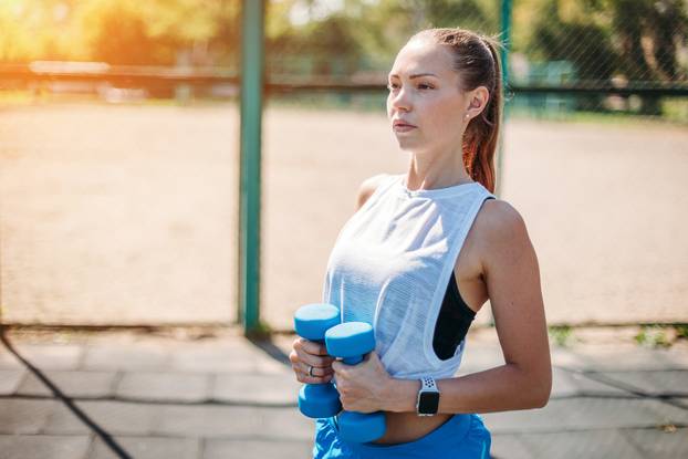 young sexy woman working out with dumbbells in the gym outdoors
