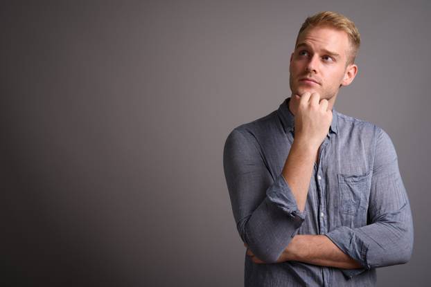 Young handsome businessman with blond hair against gray backgrou