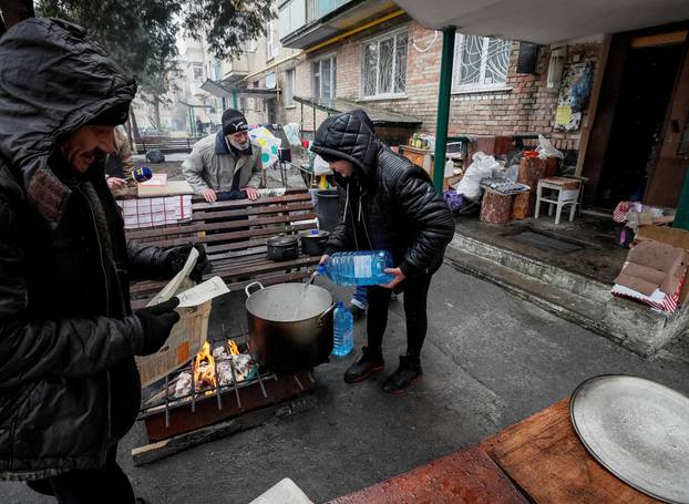 Locals residents cook food on a fire in the yard of their house in Bucha