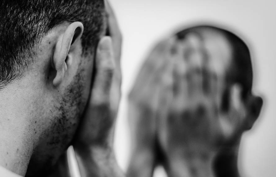 A man is looking into the mirror and covering his face 