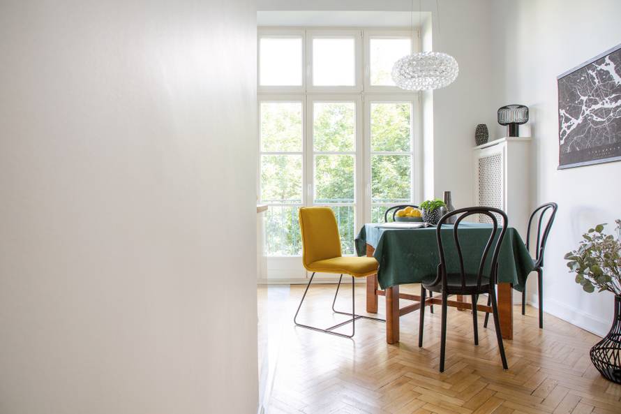 Table with dark green tablecloth, magazine, fresh lemons and plant in real photo of white dining room interior with herringbone parquet, glass lamp and balcony. Empty wall with place for your graphic