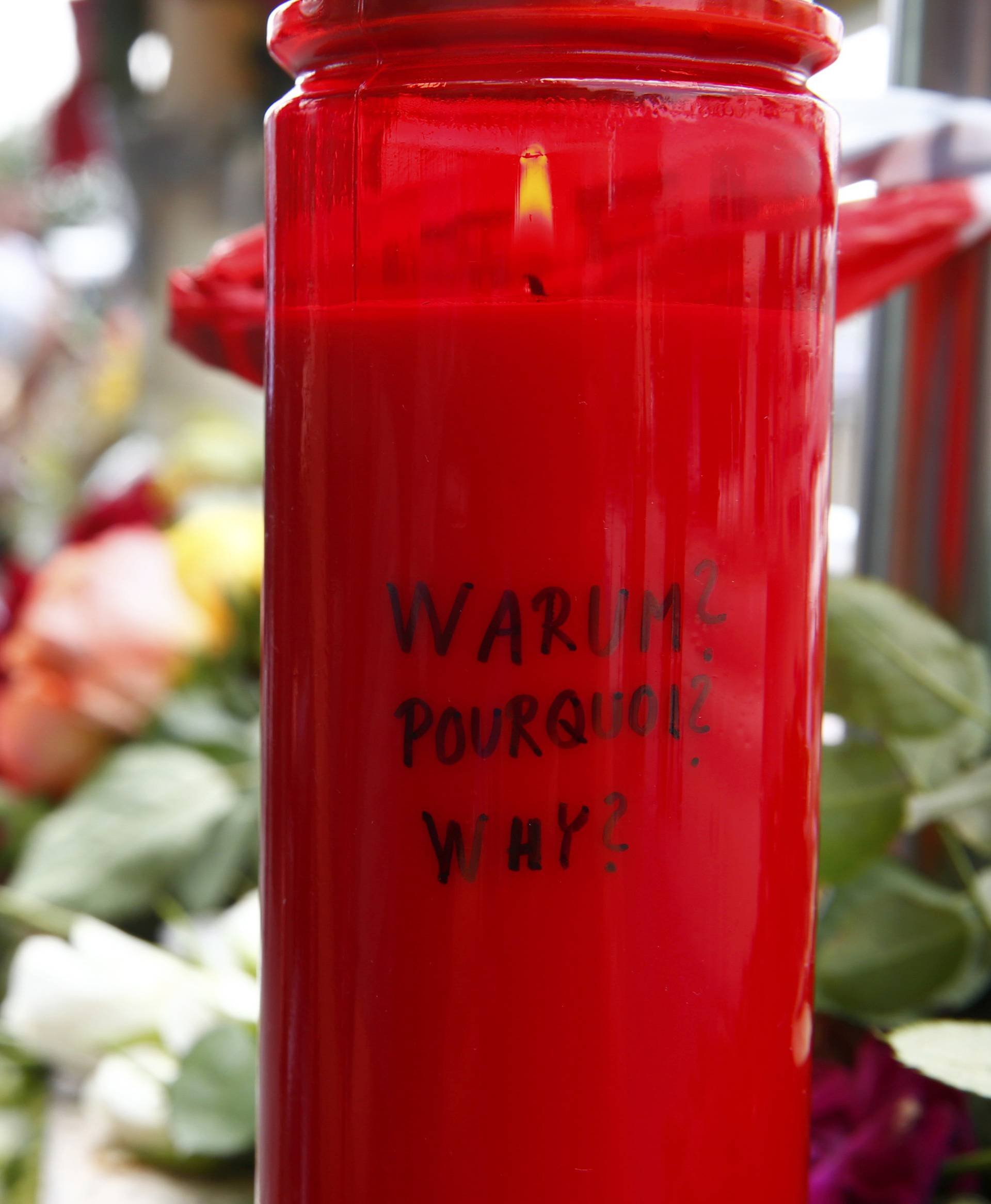 A candle with the words 'Why?' written upon it is placed next to flowers near Olympia shopping mall in Munich
