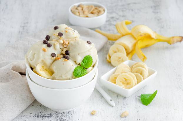 Homemade vegan banana ice cream in a bowl with peanuts and chocolate on a wooden background. Healthy dessert. Horizontal, copy space.