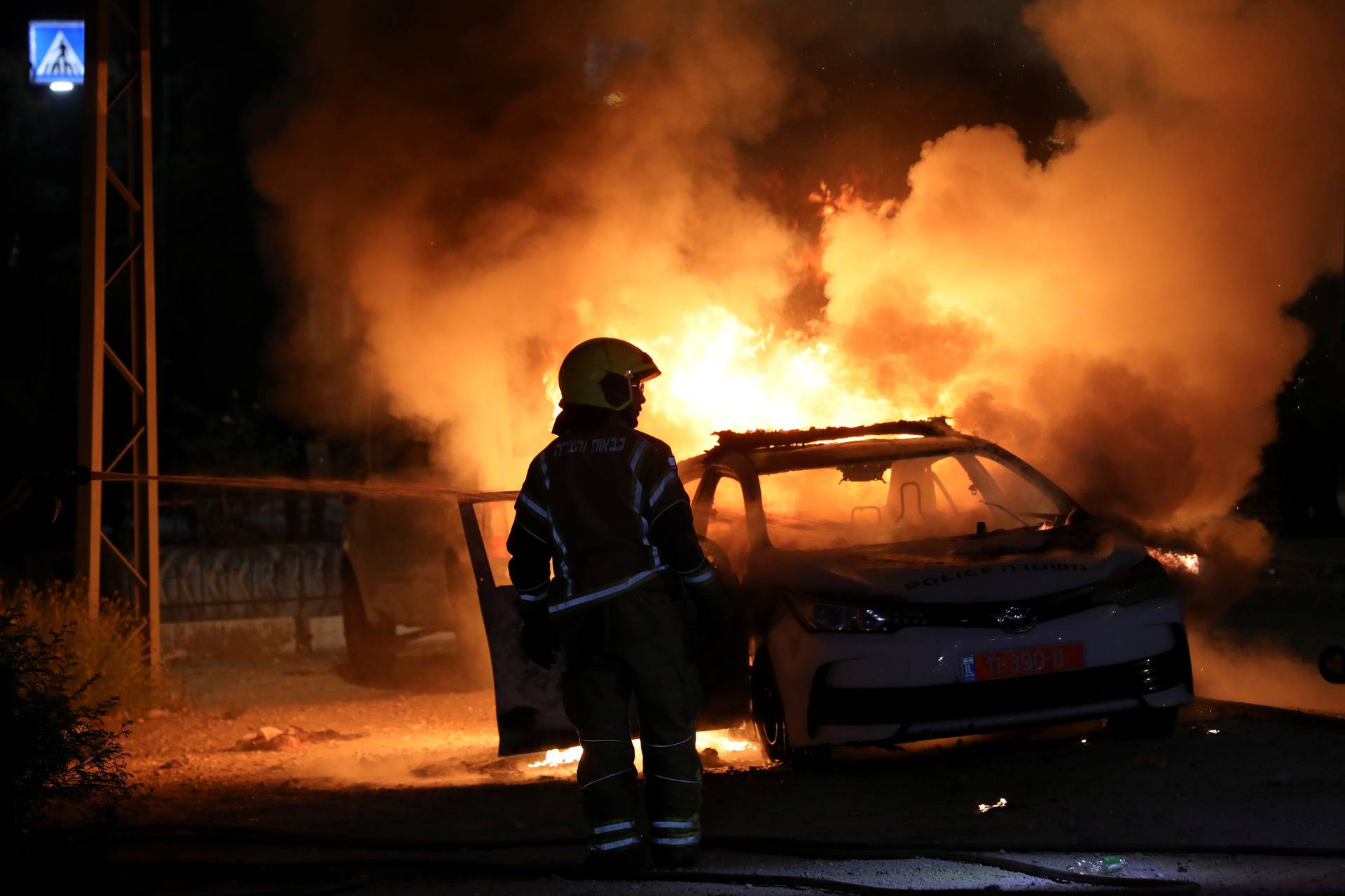 An Israeli firefighter stands near a burning Israeli police car during clashes between Israeli police and members of the country's Arab minority in the Arab-Jewish town of Lod